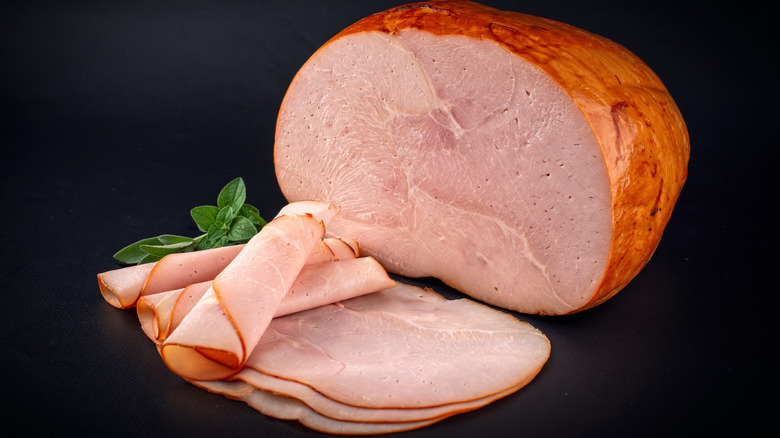A large ham with slices in front of it.