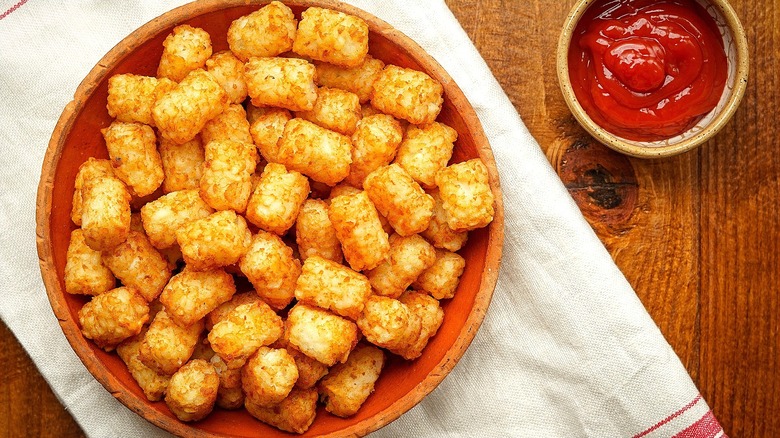 Top-down view of tater tots in a wooden bowl next to a small bowl of ketchup