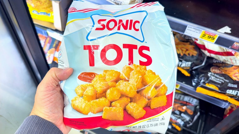 Hand holding a bag of Sonic tots in the freezer section of a supermarket