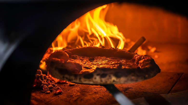A traditional Neapolitan pizza being taken out of the oven, showing the classic "leoparding"