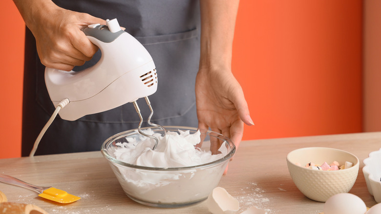 A person whipping egg whites in a glass bowl with an electric mixer.