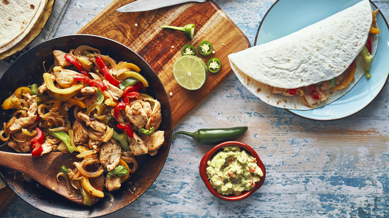 A pan of meat and veggies for fajitas beside a plated filled tortilla.