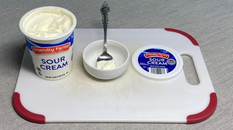 Container of Friendly Farms sour cream on a cutting board.