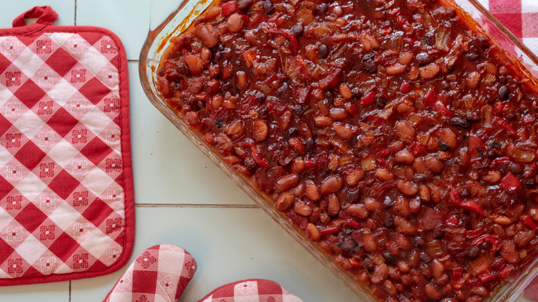A tray of baked beans with oven mitts on the side