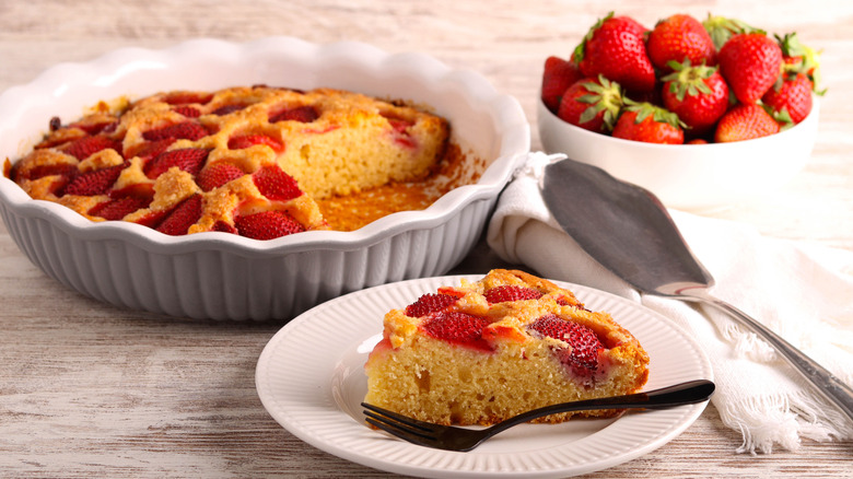 A strawberry cornmeal cake in a dish with a plated slice of cake and bowl of strawberries