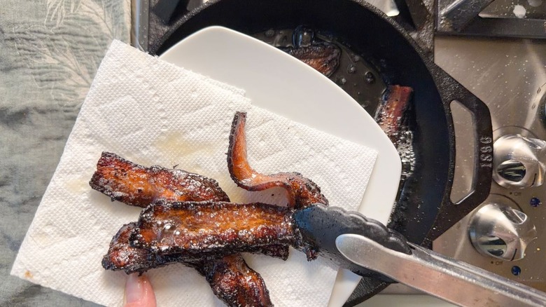 Placing cooked bacon strips on paper towel with tongs