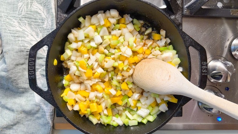 Chopped peppers, onion, and celery in cast iron skillet with wooden spoon