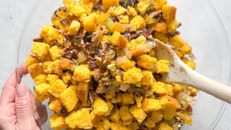 Stirring cornbread dressing ingredients in glass bowl with wooden spoon