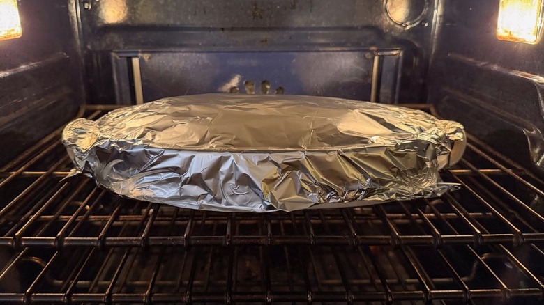 Southern-style homemade cornbread dressing in foil covered casserole dish in oven