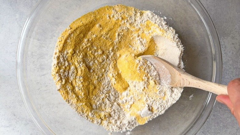 Stirring dry ingredients for cornbread in glass bowl with wooden spoon