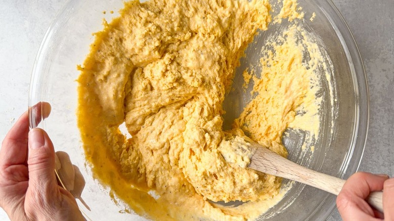 Mixing cornbread batter in glass bowl with wooden spoon