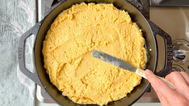 Spreading cornbread batter in cast iron skillet with offset spatula