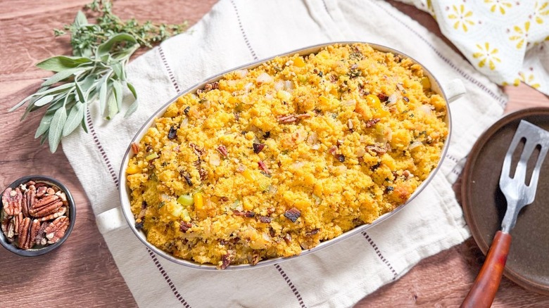 Southern-style homemade cornbread dressing in serving dish on table with pecans and fresh herbs