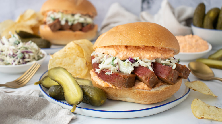 Meatloaf sandwich with pickles and chips on plate