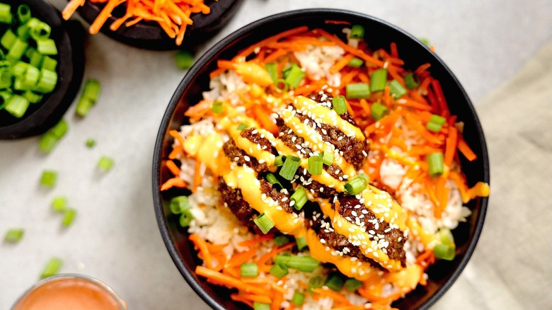 Marinated salmon topped with spicy mayonnaise over white rice with shredded carrots and chopped green onions in a black bowl