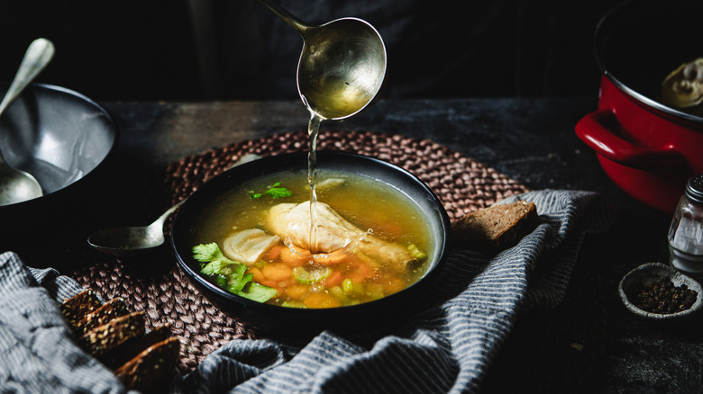 Cropped shot of pouring soup in bowl using ladle. Serving chicken broth in soup bowl over kitchen counter.