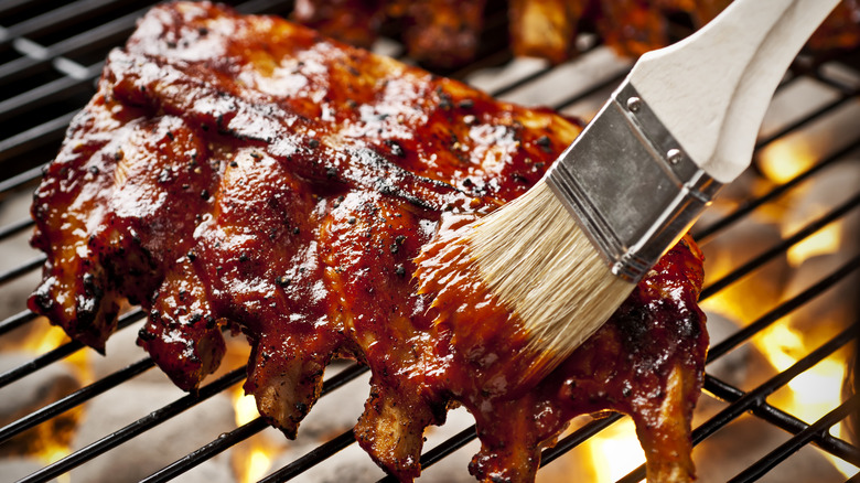 Baby back ribs on grill with sauce being painted on with basting brush