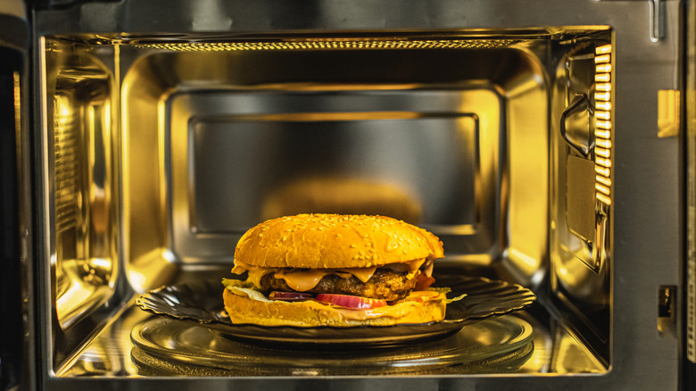 An open oven revealing a juicy burger sitting on a plate, ready to be reheated.