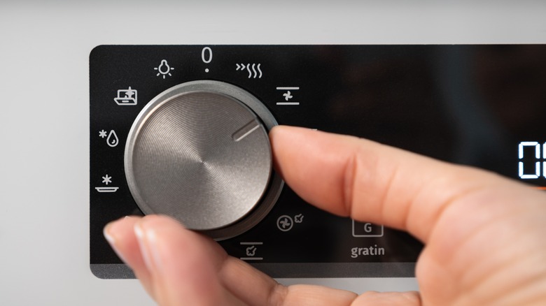 A hand adjusting the settings on the oven's knob.
