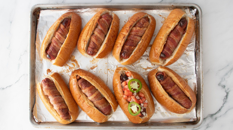 Bacon-wrapped hot dogs in buns with one topped with tomato and jalapeno