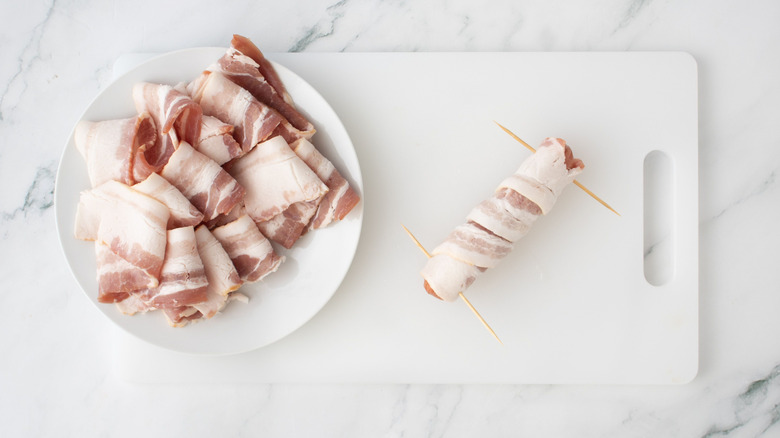Bacon slices on plate next to hot dog wrapped in bacon