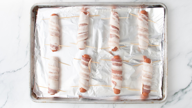 Bacon-wrapped hot dogs on baking sheet