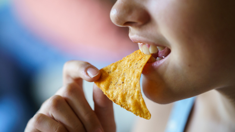 A woman takes a bite of a tortilla chip