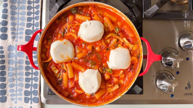 Burrata halves in tteokbokki in red pan on stovetop