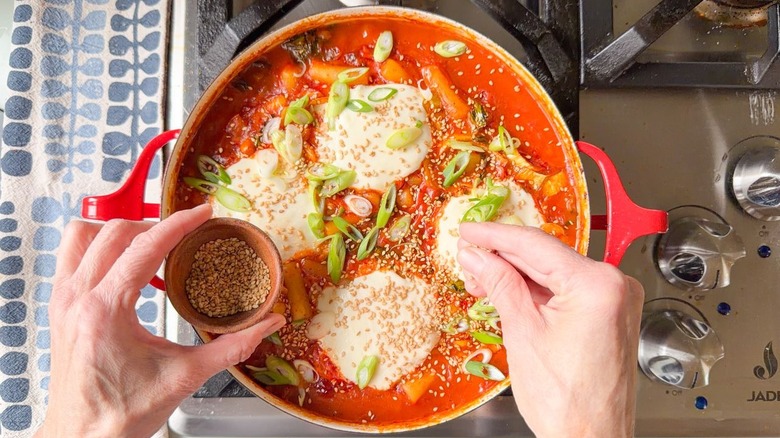 Sprinkling sesame seed on spicy baked tteokbokki in red pan on stovetop