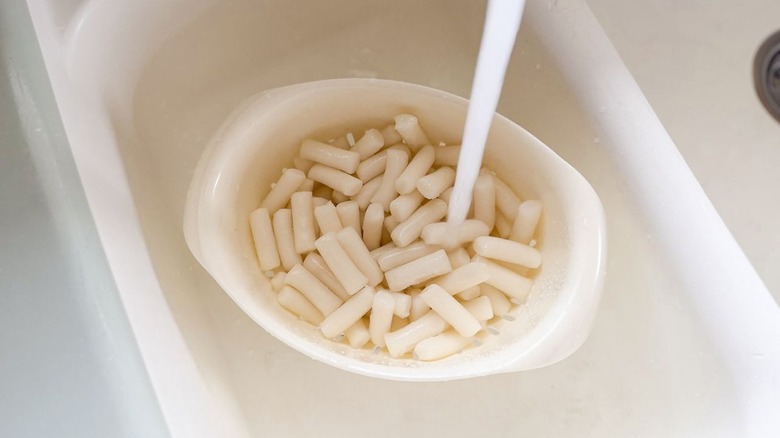 Rice cakes under running water in colander in sink