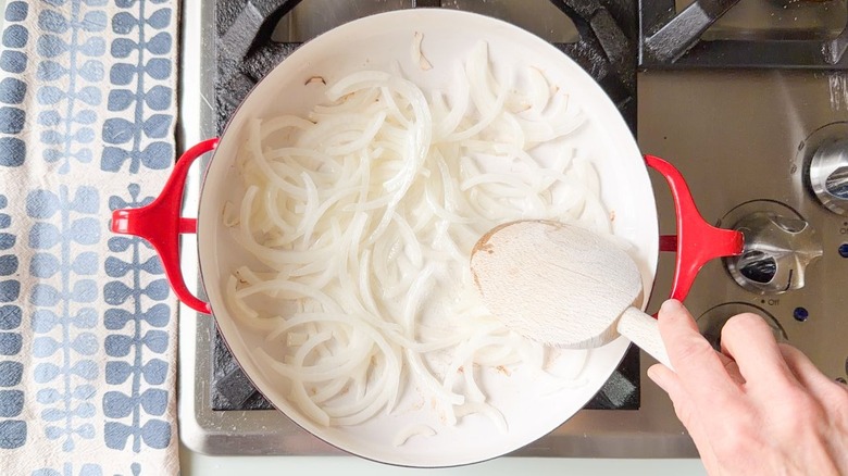 Sliced white onion cooking in peanut oil in red pan on stovetop