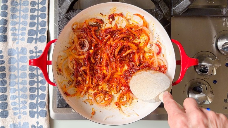 Cooking sliced onion with garlic, gochujang, gochugaru, bonito flakes, and sesame oil in red pan on stovetop