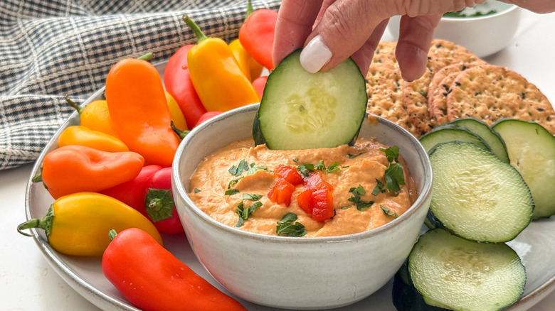 hand dipping cucumber into hummus