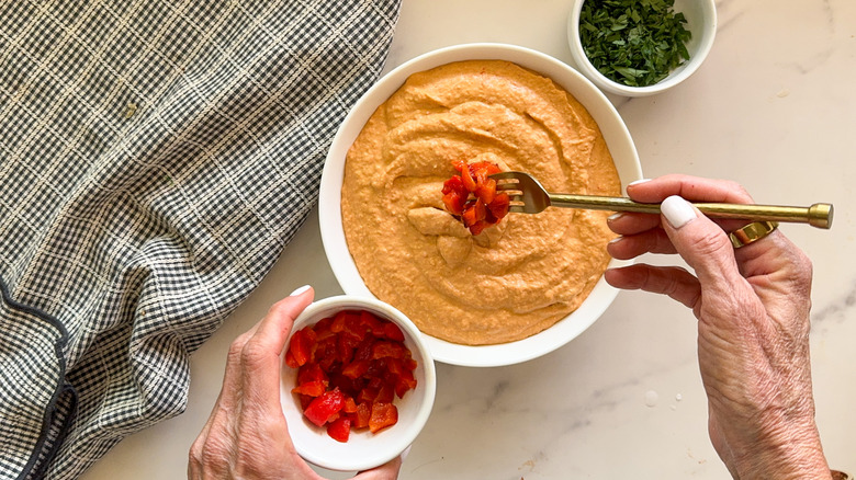 hand adding peppers to hummus
