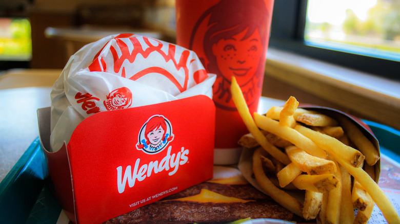 A wrapped Wendy's sandwich with fries and a drink on a tray.
