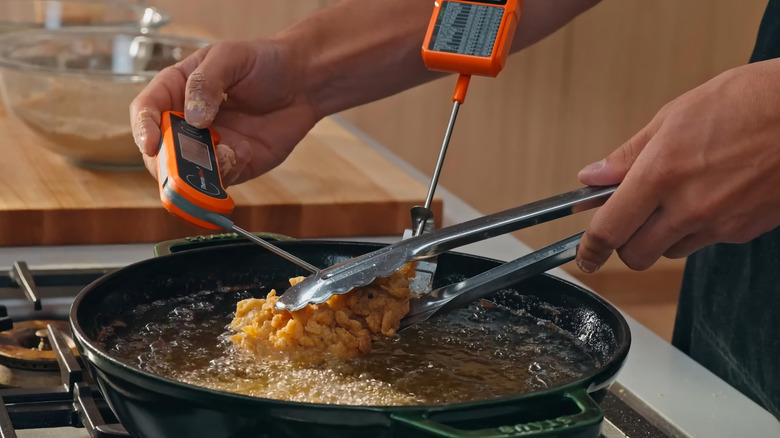 Person checking the temperature of chicken they're deep-frying on the stove