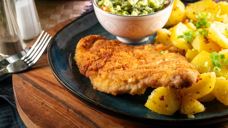 A breaded pork chop on a plate beside potatoes.