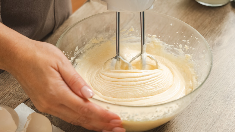 Person mixing a batter in a clear mixing bowl with a hand mixer