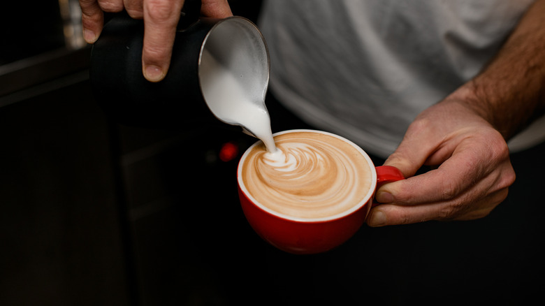 A person making latte art on a small red cup of coffee.