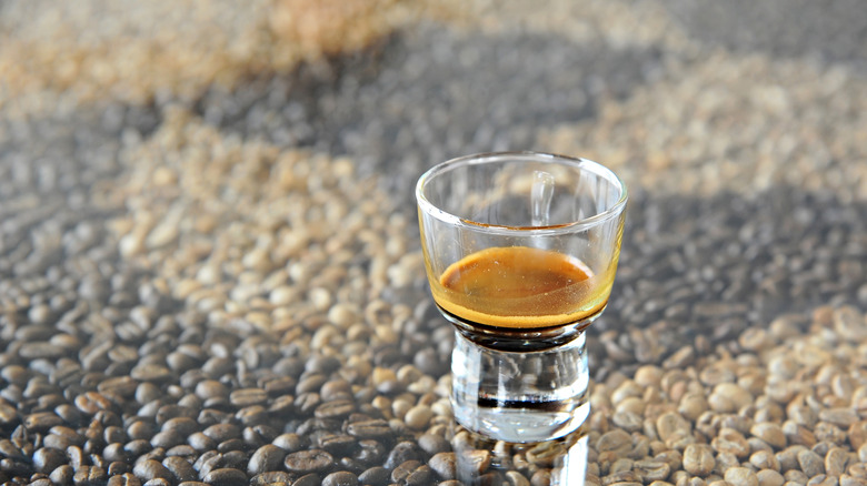 A shot of ristretto in a glass, set against coffee beans as background.