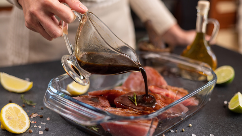 A person pouring a dark sauce into a steak in a glass casserole dish