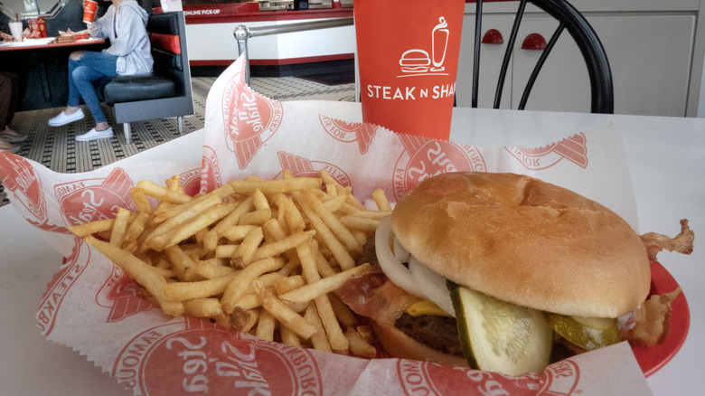 A fast food burger on a tray with a drink and fries on the side.