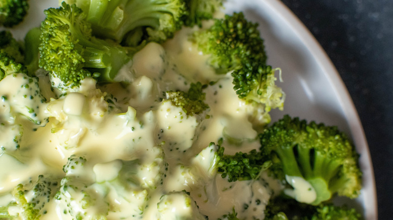 Close-up of broccoli florets covered in hollandaise sauce on a white plate