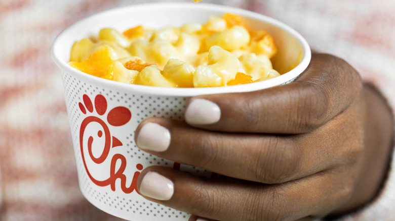Person's hand with pink pained fingernails holding a cup of Chick-fil-A mac and cheese