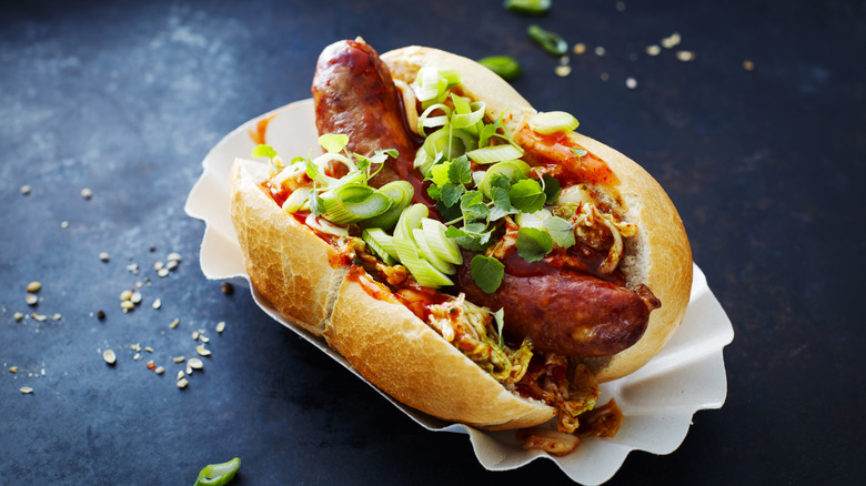 hot dog topped with spring onions and ketchup on a black background