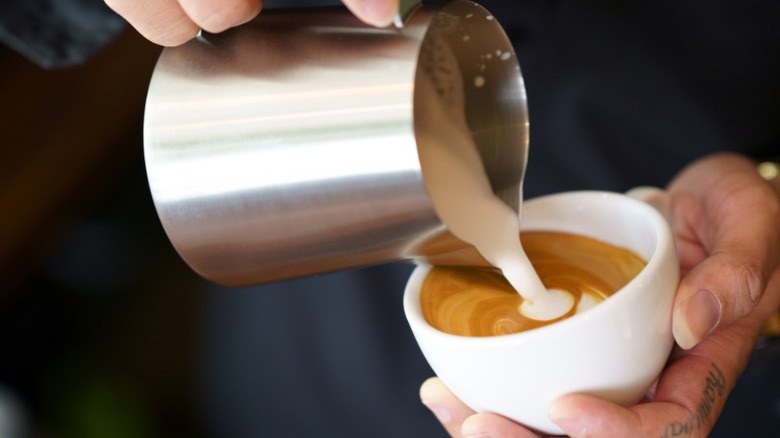 A person pouring steamed milk into a mug with coffee in it