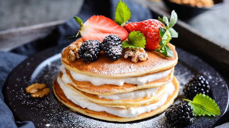 Pancakes layered with whipped cream and topped with fresh berries, walnuts, and powdered sugar