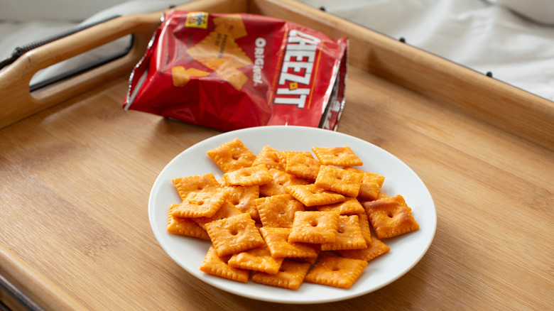 Cheez-Its on a white plate next to an empty Cheez-Its bag on a wooden serving tray