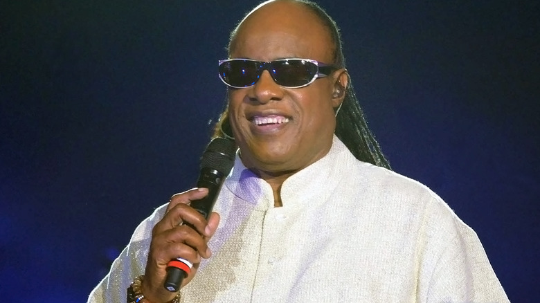 Stevie Wonder holding a microphone against a dark blue background.