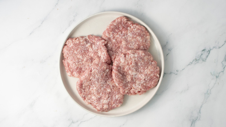 Raw pork patties seasoned with salt on a white plate